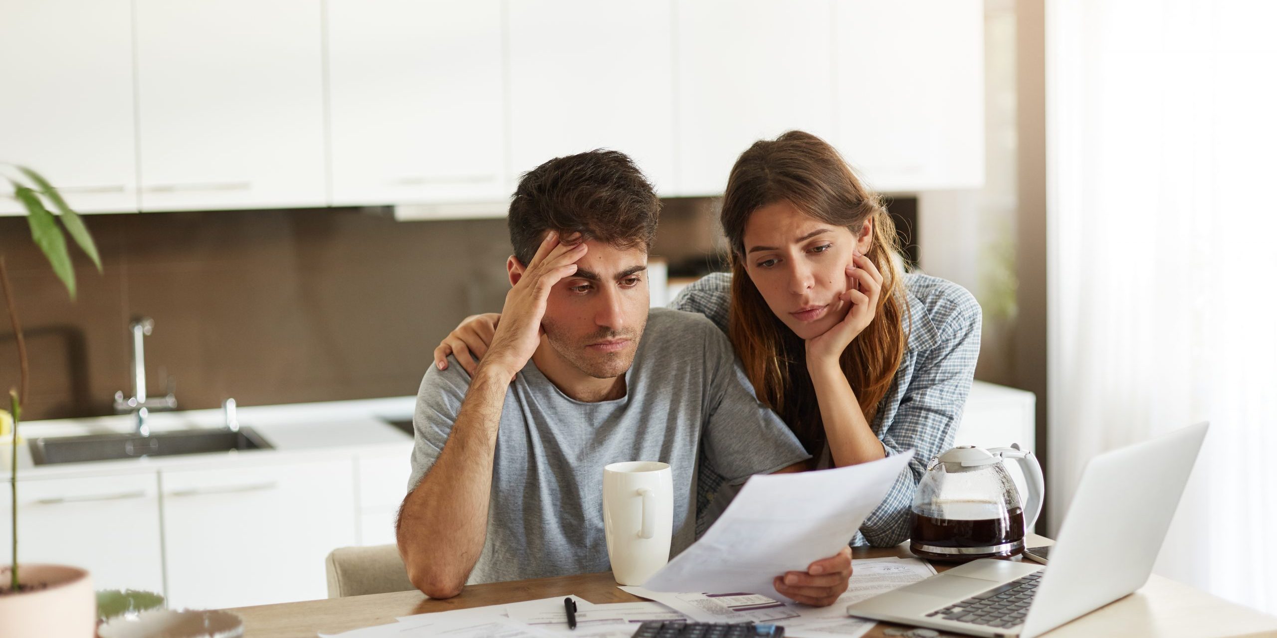 Unhappy American couple managing home accounts in kitchen, trying to save some money by cutting family expenses. Finances, bankruptcy, taxes, money, accounting and financial problems concept